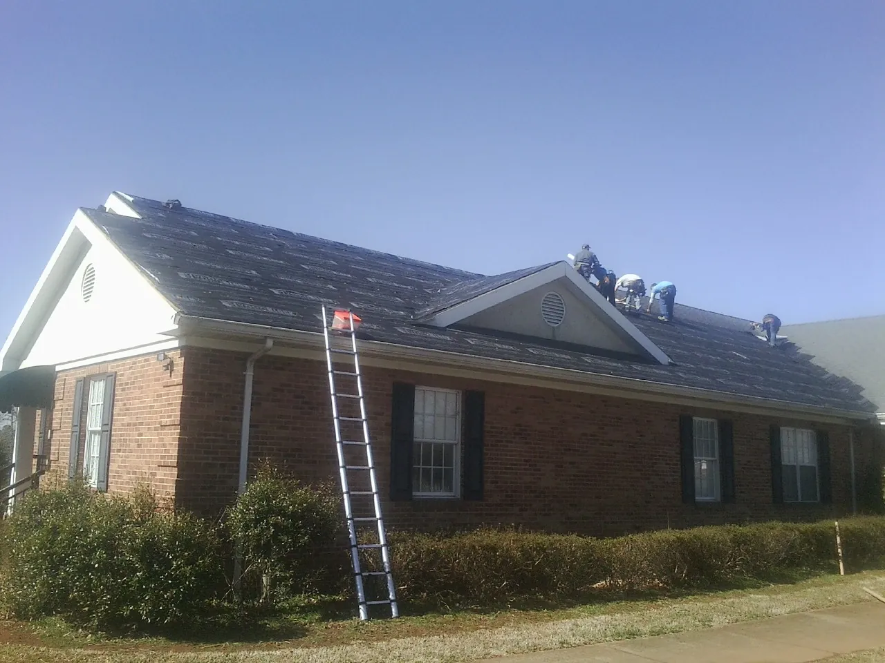 Crew tearing shingles off a brick ranch roof with a ladder set — Emergency Roof Repair work by our crew in Lyndhurst