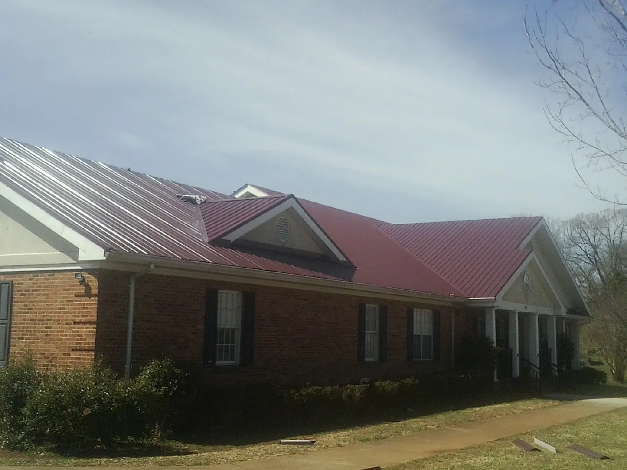 Red metal roof with gabled entries on a long brick building, from a Hail Damage Roof Repair job in Lyndhurst