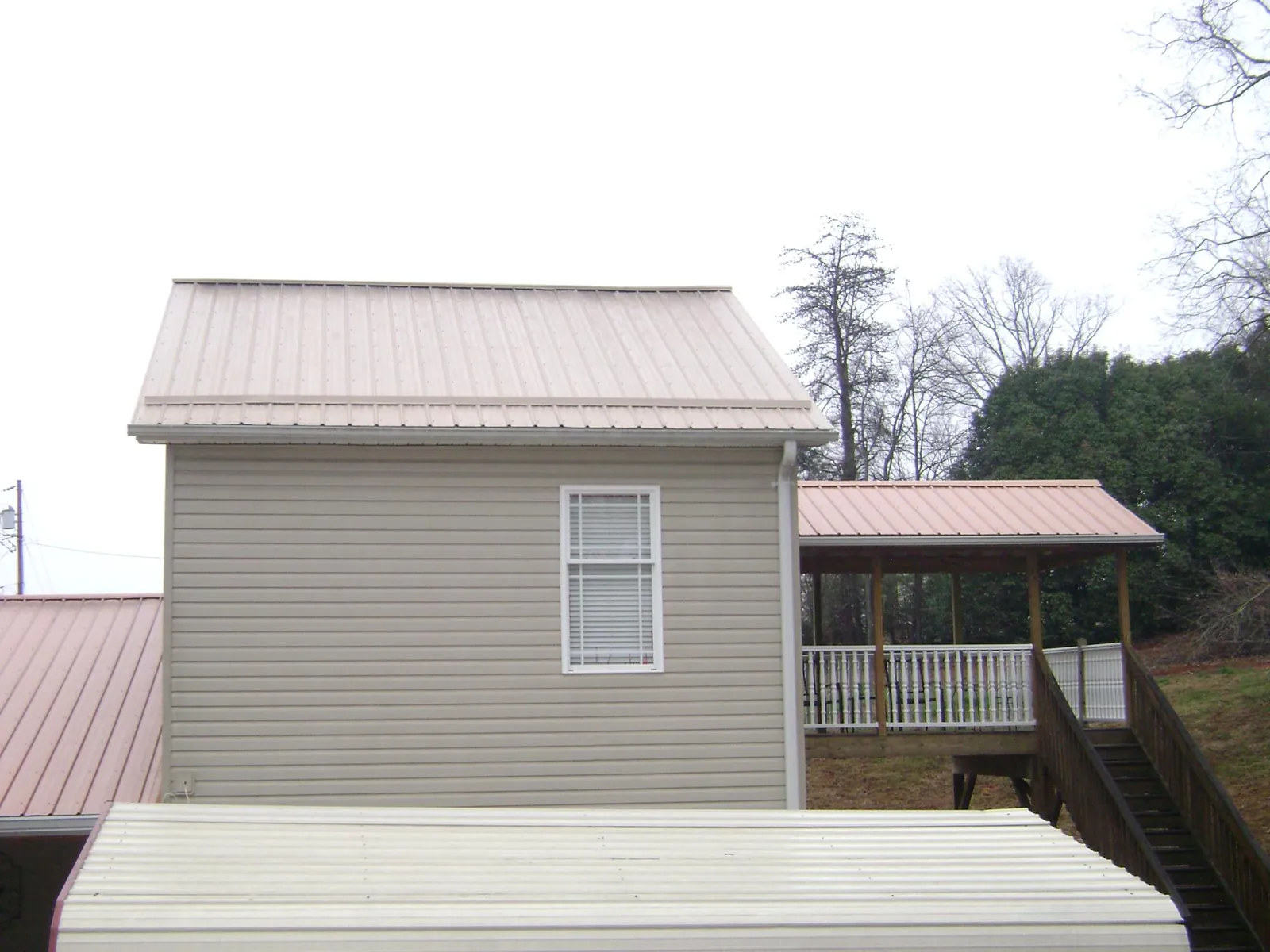 Tan metal roofs on a two story addition and attached porch, from a Roof Replacement job in Lyndhurst